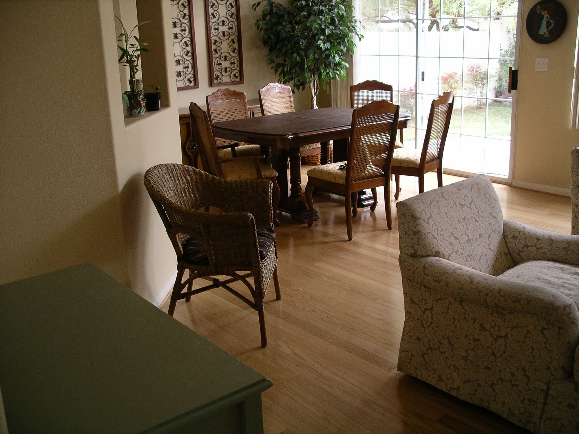 Dining room with wooden table and chairs, light sofa, and green cabinet by a sunlit window.