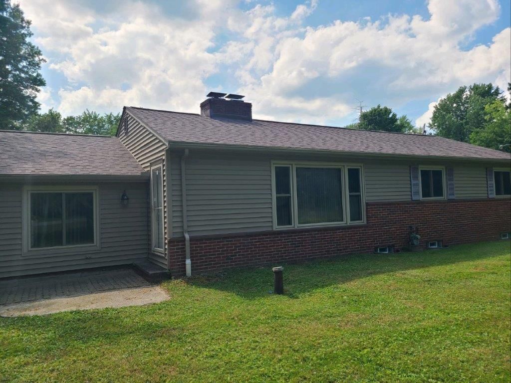 A house with a roof and a lot of windows is sitting on top of a lush green field.