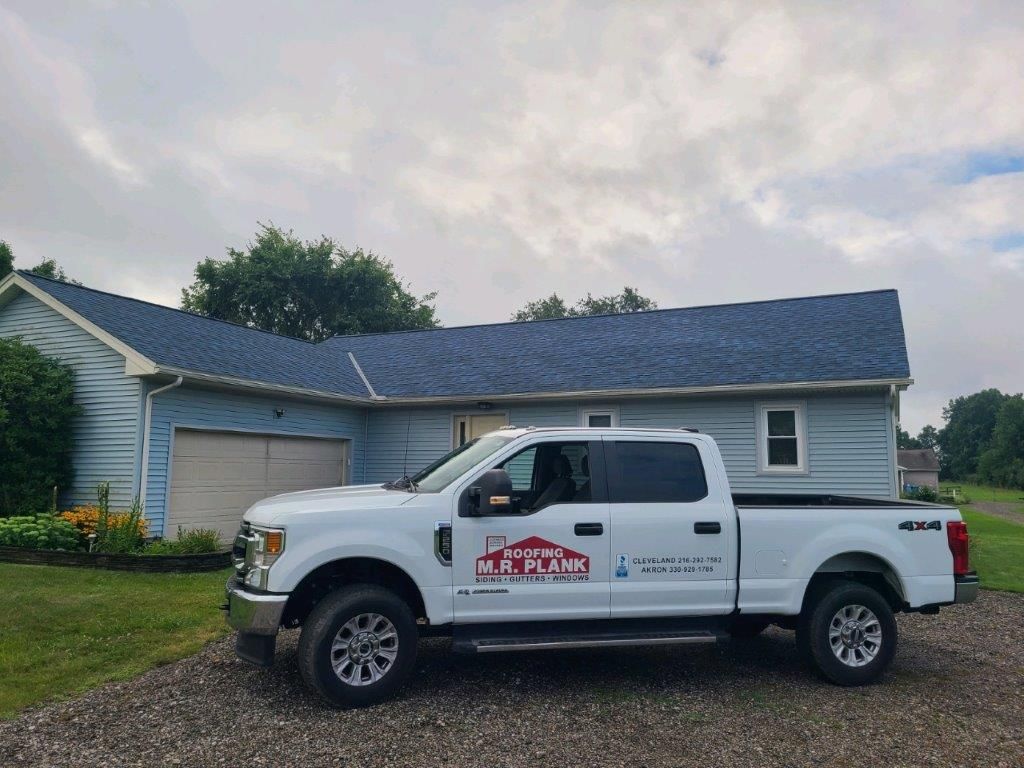 A white truck is parked in front of a house with a blue roof.