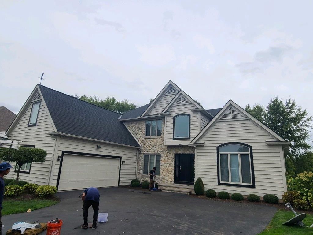 A man is standing in front of a large white house with a black roof.