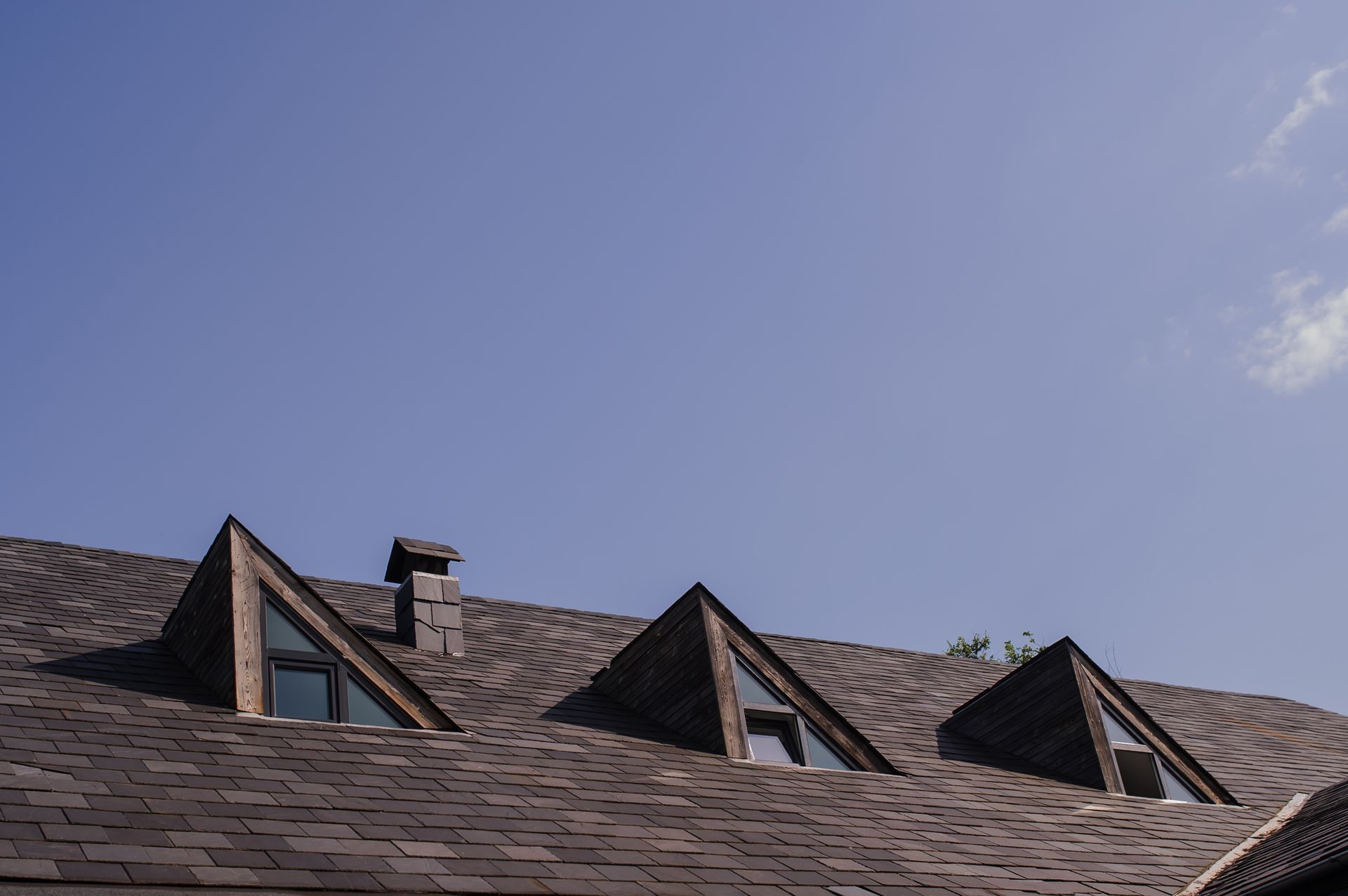 A roof with three windows and chimneys on it against a blue sky.