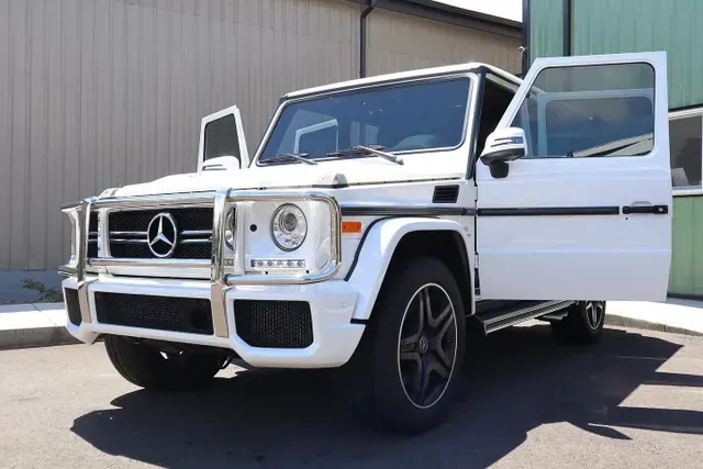 A white mercedes with its doors open is parked in front of a building.