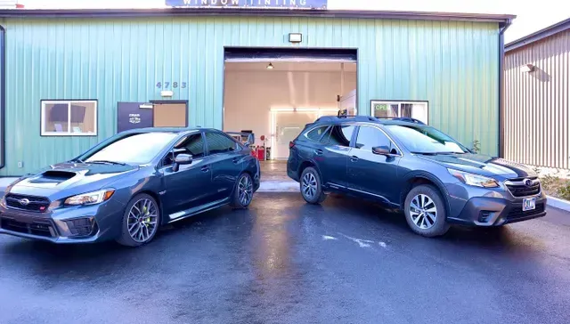 Two cars are parked in front of a green building.