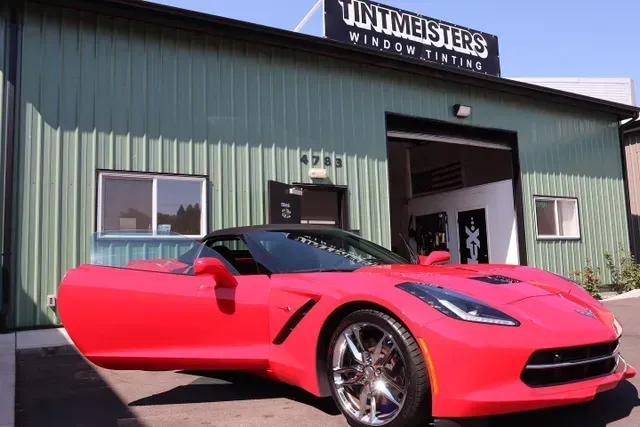 A red sports car is parked in front of a tintmeisters building