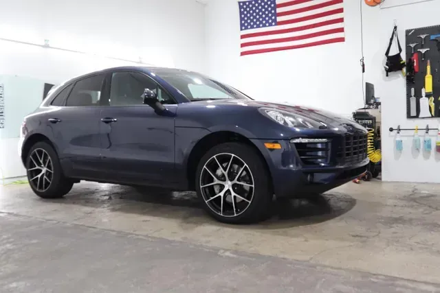 A blue porsche macan is parked in a garage next to an american flag.