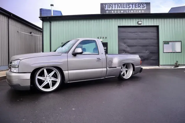 A silver truck is parked in front of a building that says tintmeisters