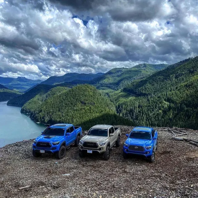 Three trucks are parked on top of a hill overlooking a lake.
