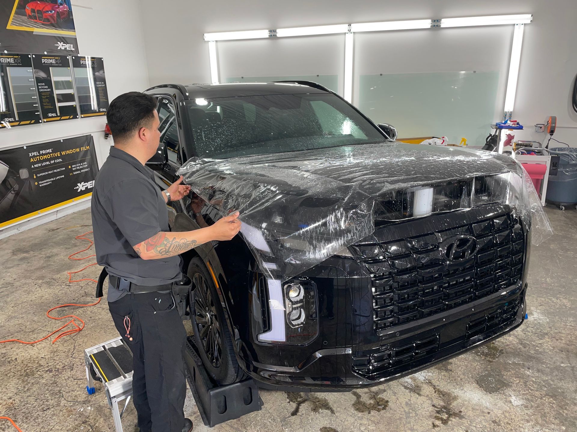 TINTMEISTERS applying clear bra AKA stone guard on the hood of a black Hyundai Palisade in a garage - Salem, OR