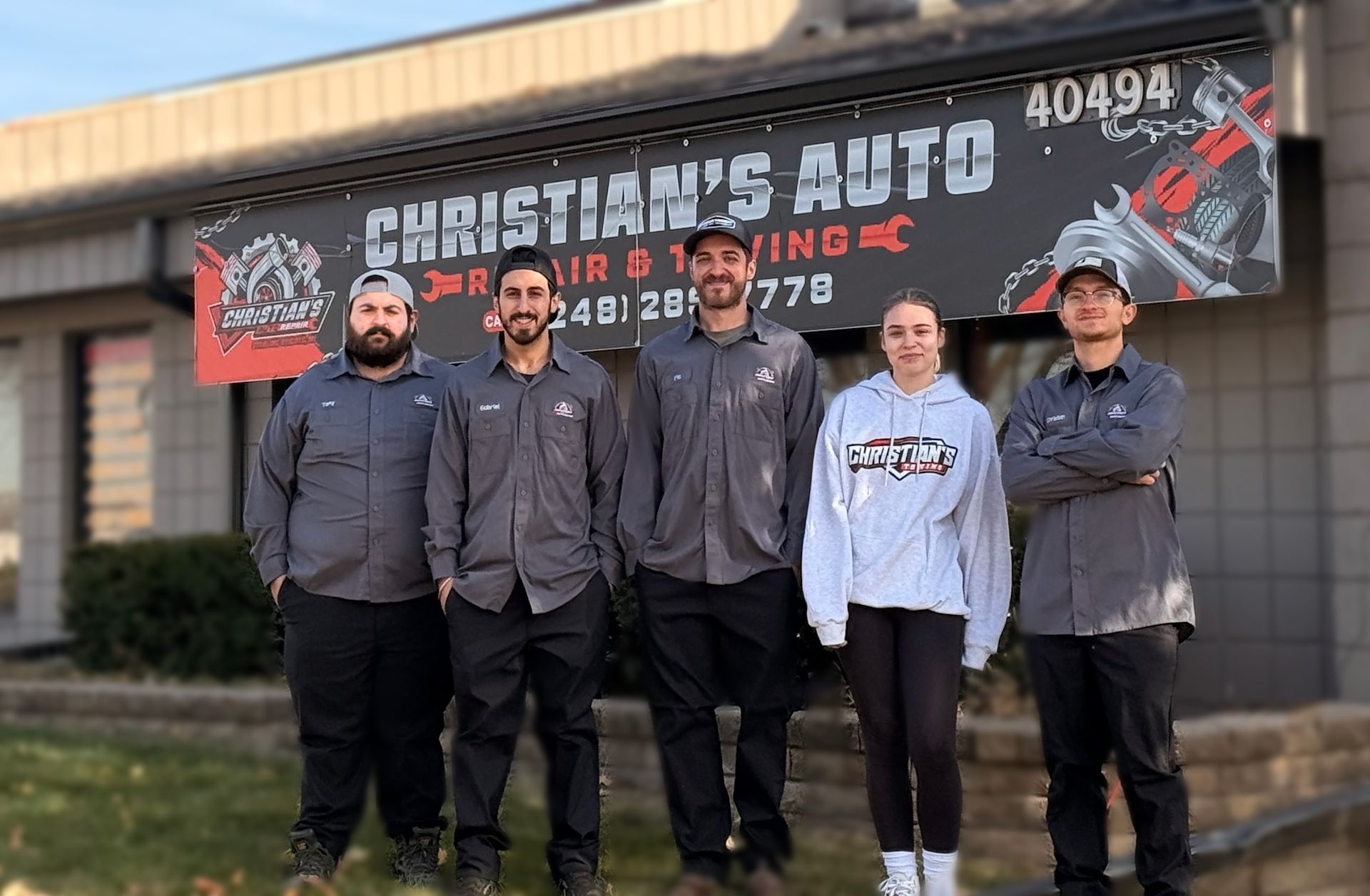 Five people in uniforms and casual clothing stand smiling in front of a Christian's Auto Repair & Towing business sign. | Christian's Auto Repair