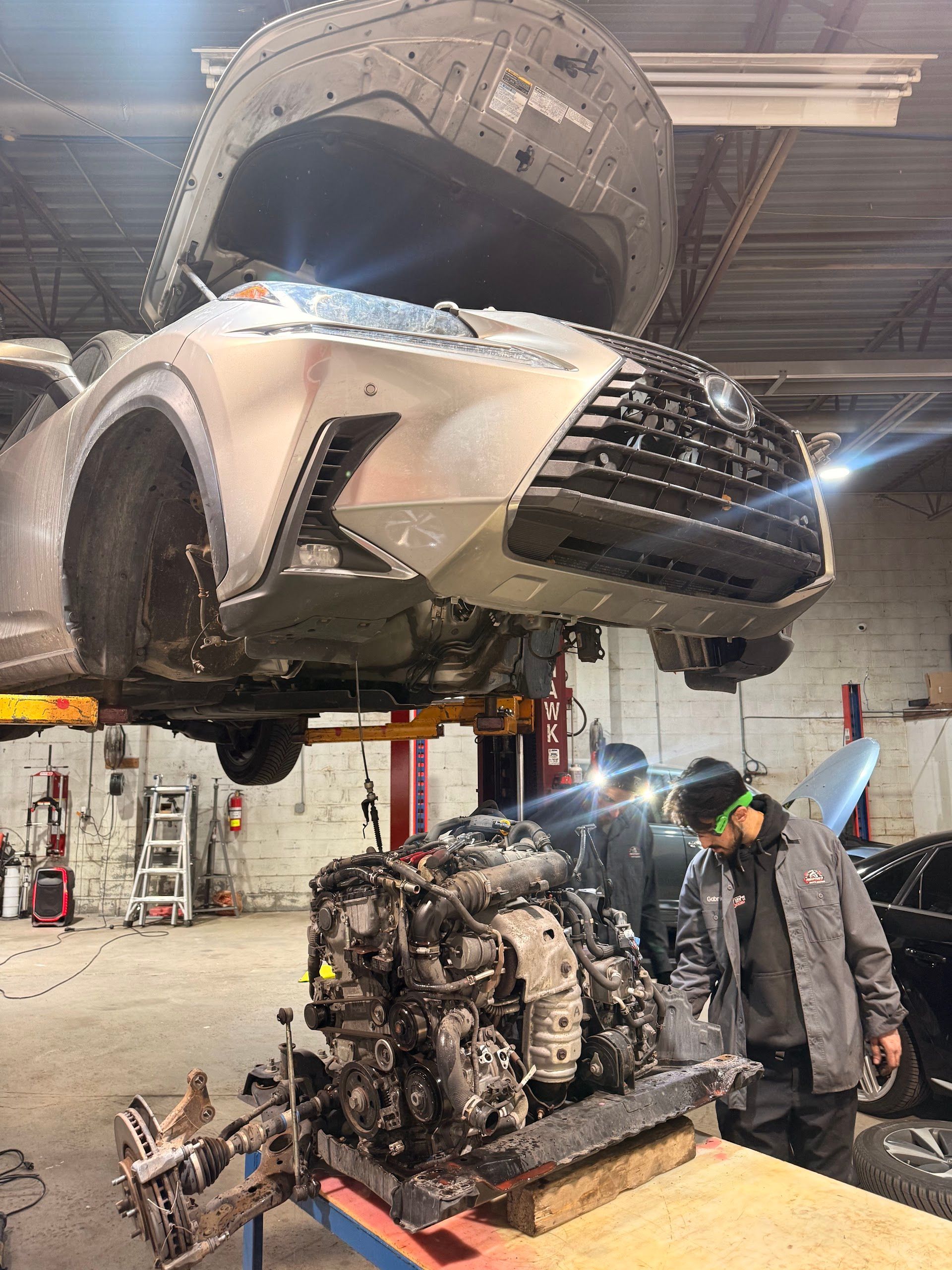 A mechanic working on an engine removed from a silver Lexus SUV elevated on a lift inside a professional auto shop.| Christian's Auto Repair
