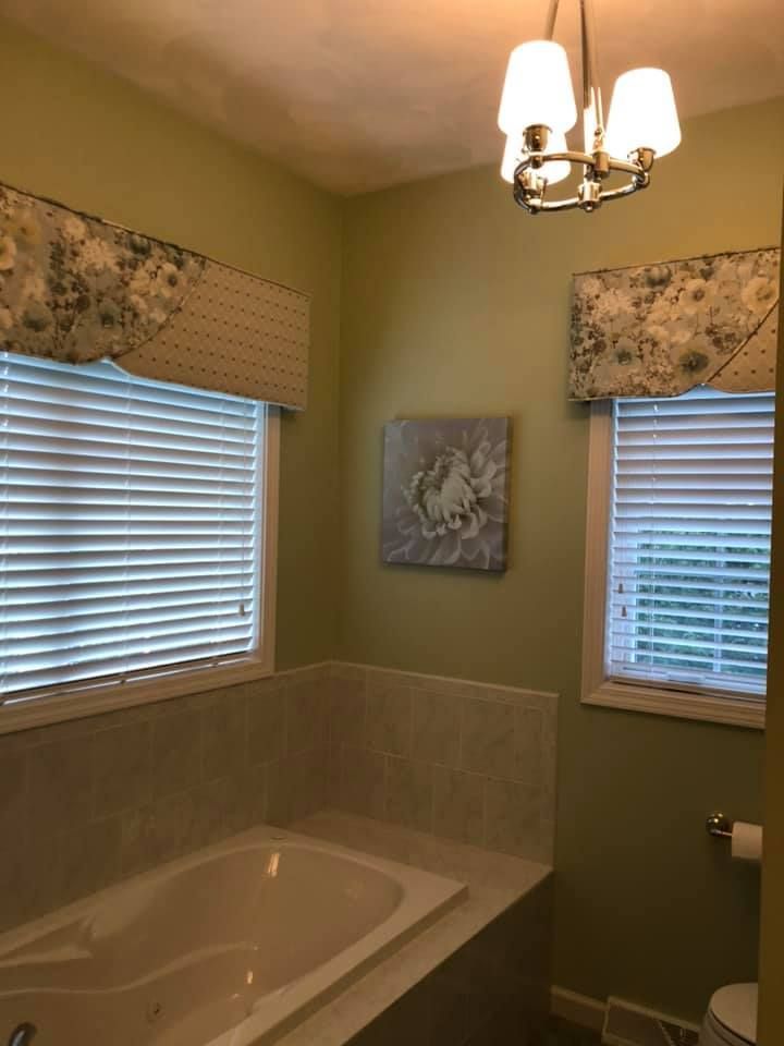 A bathroom with a tub , toilet and two windows