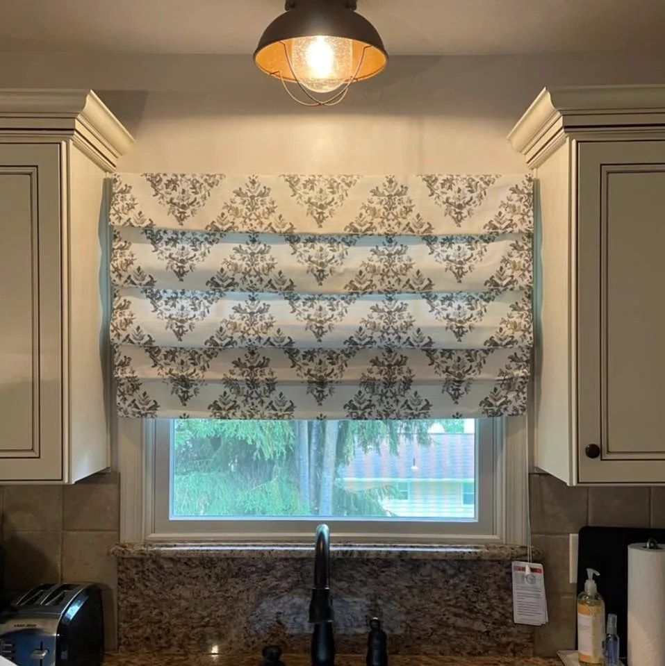 A kitchen with a sink and a window with a roman shade