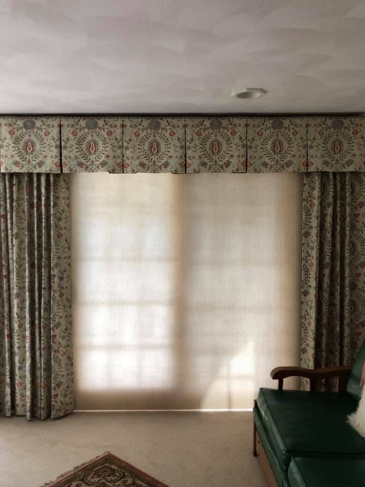 A living room with a green chair , curtains and blinds.