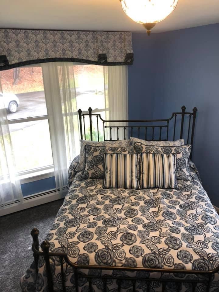 A bedroom with a bed and a window with a car parked in the background.