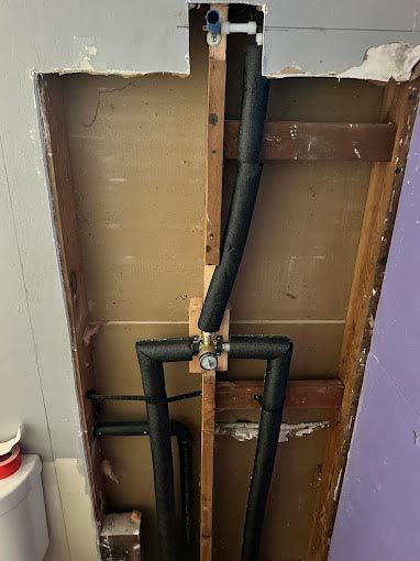 A bathroom with a hole in the wall and pipes coming out of it.