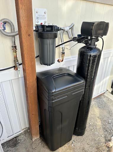 A water softener is sitting next to a trash can on the side of a building.