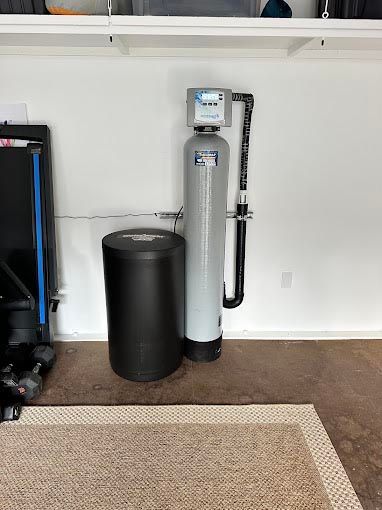 A water filter is sitting in a garage next to a black tank.
