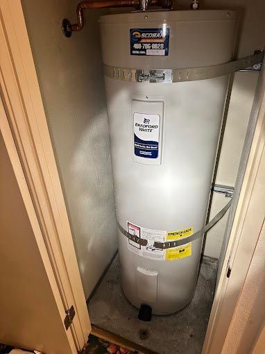 A white water heater is sitting in a closet next to a door.