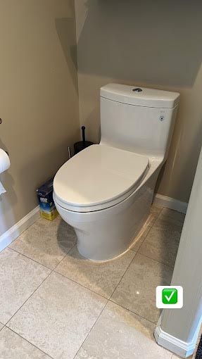 A white toilet is sitting on a tiled floor in a bathroom.