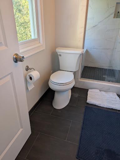 A bathroom with a toilet , shower and window.