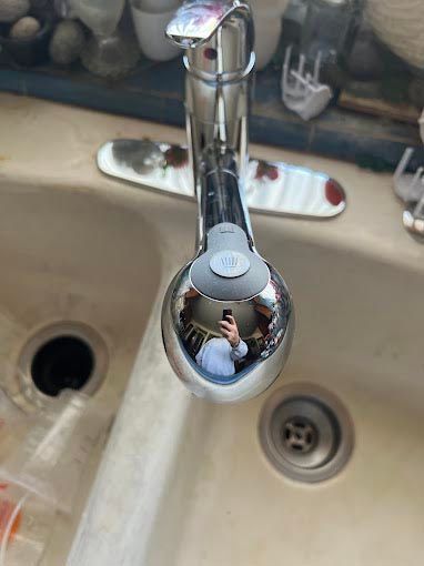 A person is taking a picture of their reflection in a sink faucet.