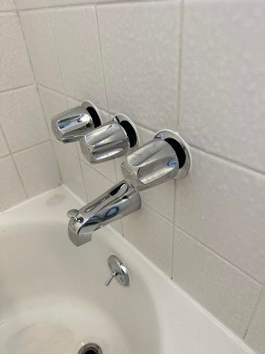 A bathroom with a bathtub and three chrome shower faucets.
