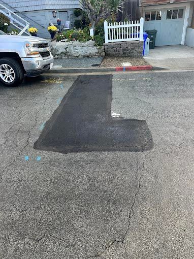 A white truck is parked on the side of the road next to a patch of asphalt.