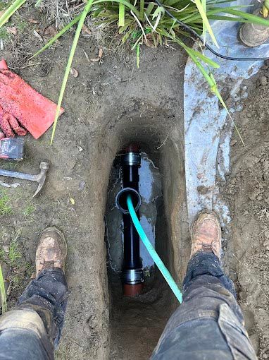 A person is standing in the dirt next to a pipe with a green hose attached to it.