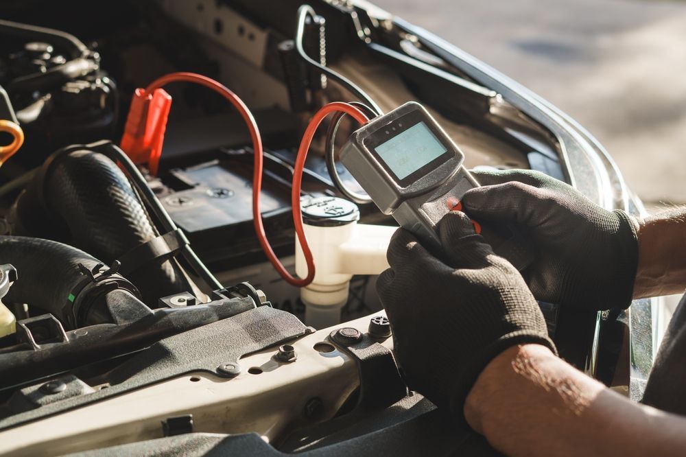 A mechanic in blue overalls holds a wrench near a white truck with its hood open for repairs.