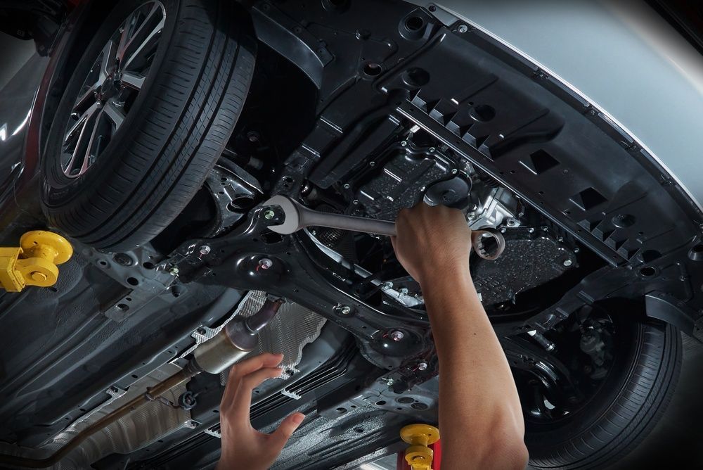 A mechanic uses a wrench to work on the underside of a vehicle lifted on a service rack.