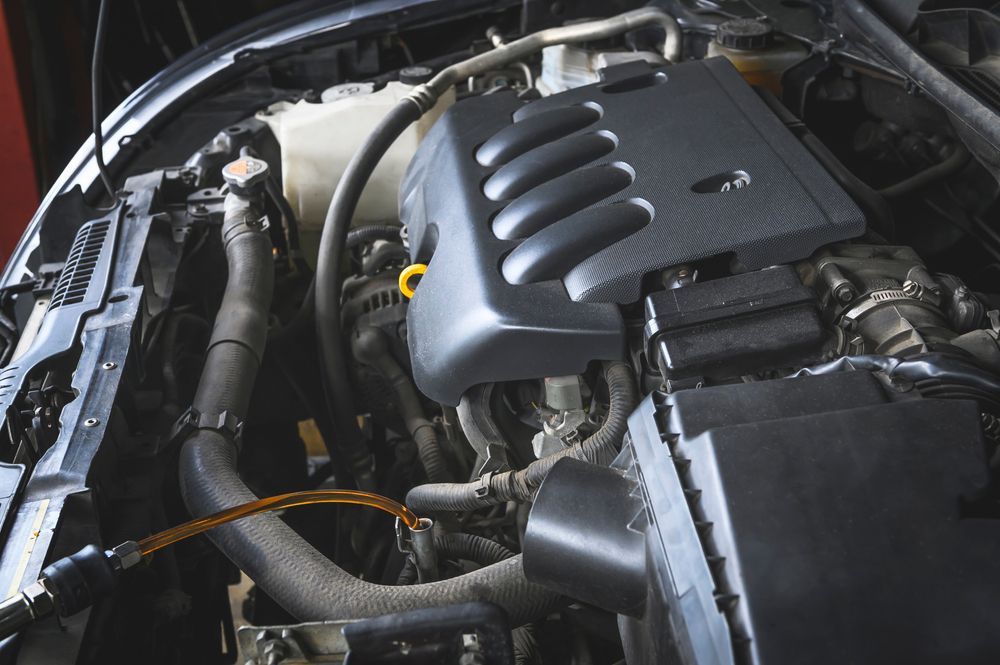 A mechanic in blue overalls holds a wrench near a white truck with its hood open for repairs.