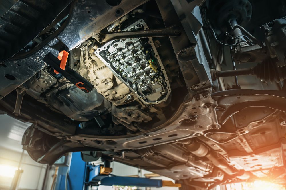 A mechanic in blue overalls holds a wrench near a white truck with its hood open for repairs.