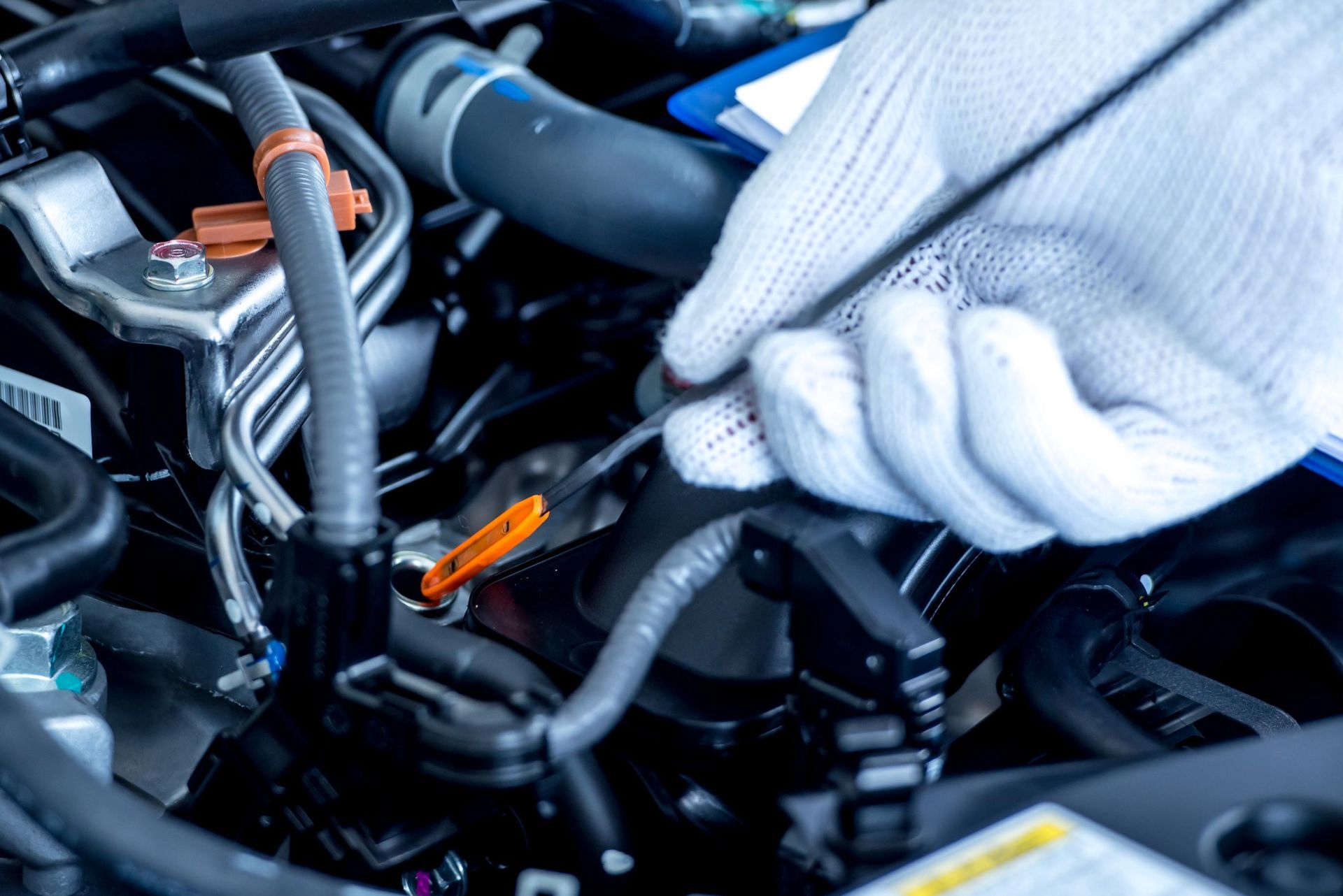 A mechanic in white gloves uses a screwdriver to perform maintenance on an open car engine.