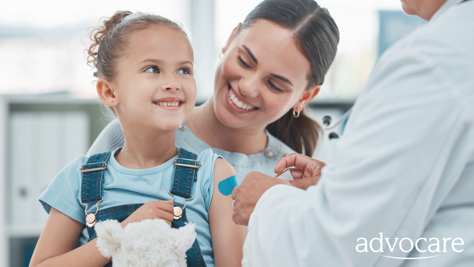 Mother holding young girl while doctor places band-aid on her arm. They are both smiling.