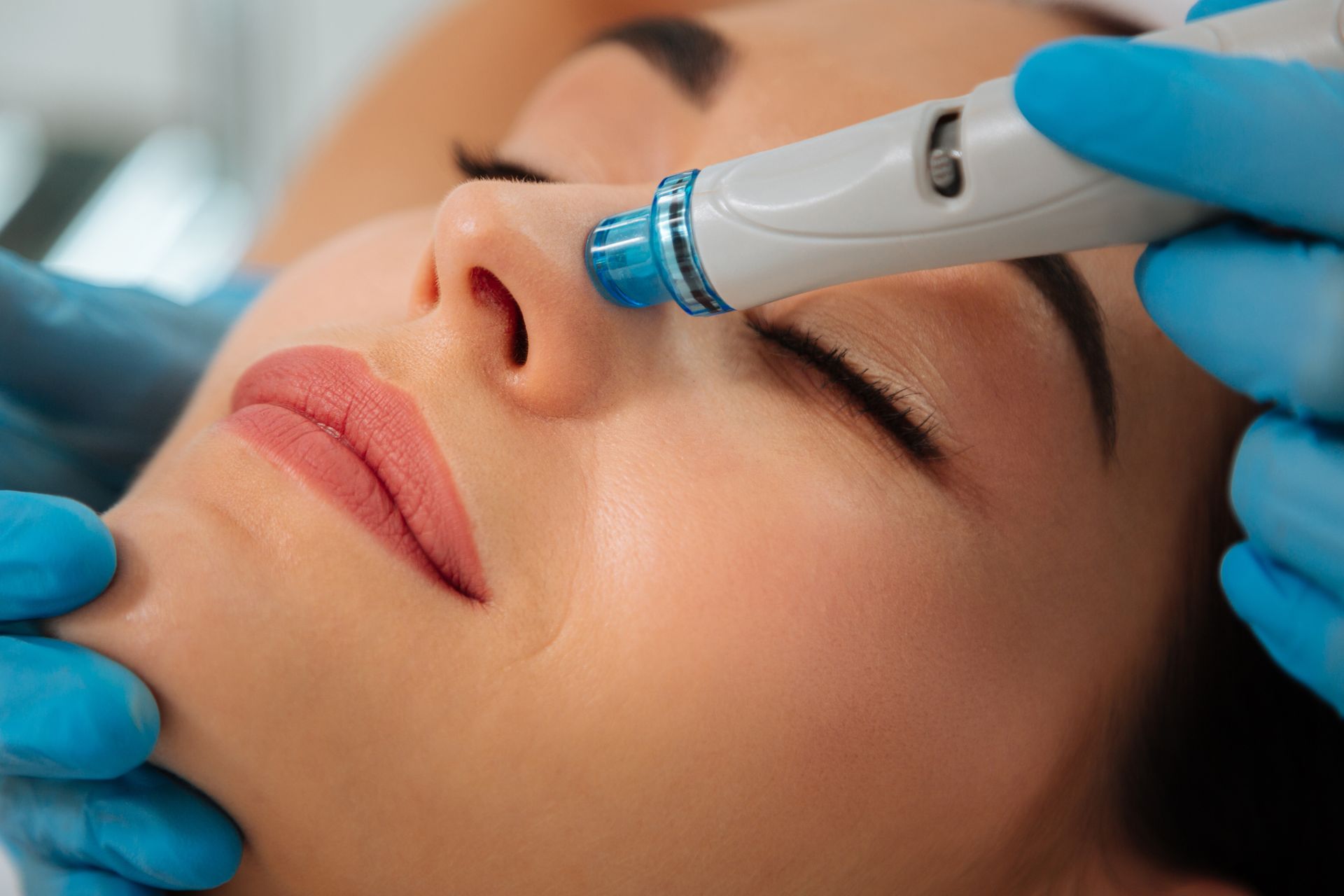 Woman receiving facial treatment with a handheld device on her nose, in a spa setting.