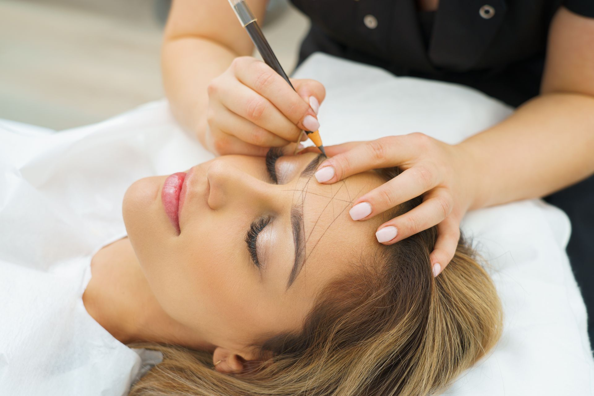 Person receiving eyebrow shaping with pencil and string on a white table.