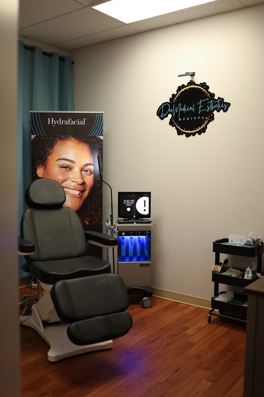 A spa treatment room featuring a reclining chair, a skincare device, a promotional banner, and a rolling utility cart.