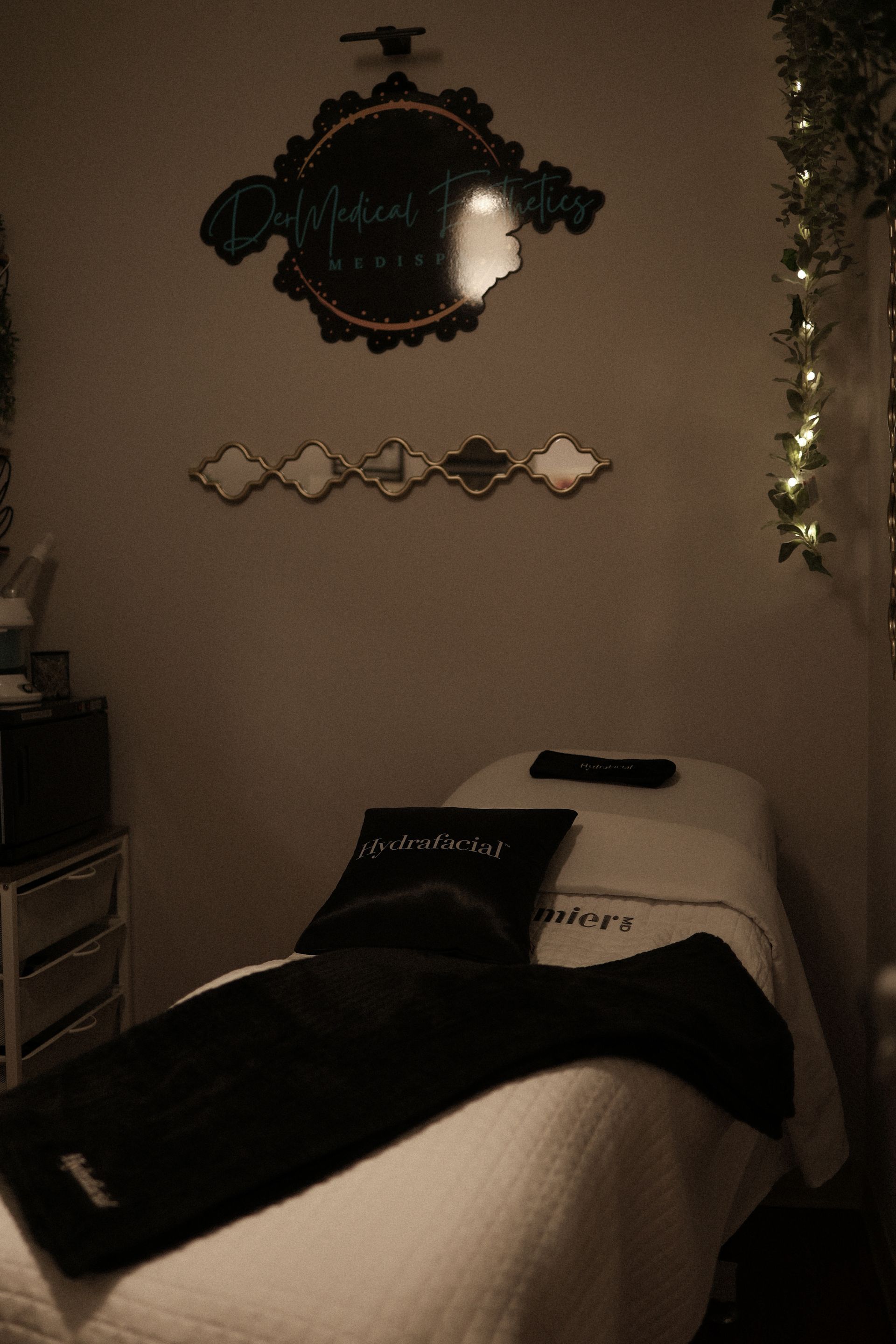 Spa treatment room with a massage table, decorative mirrors, and hanging vines.