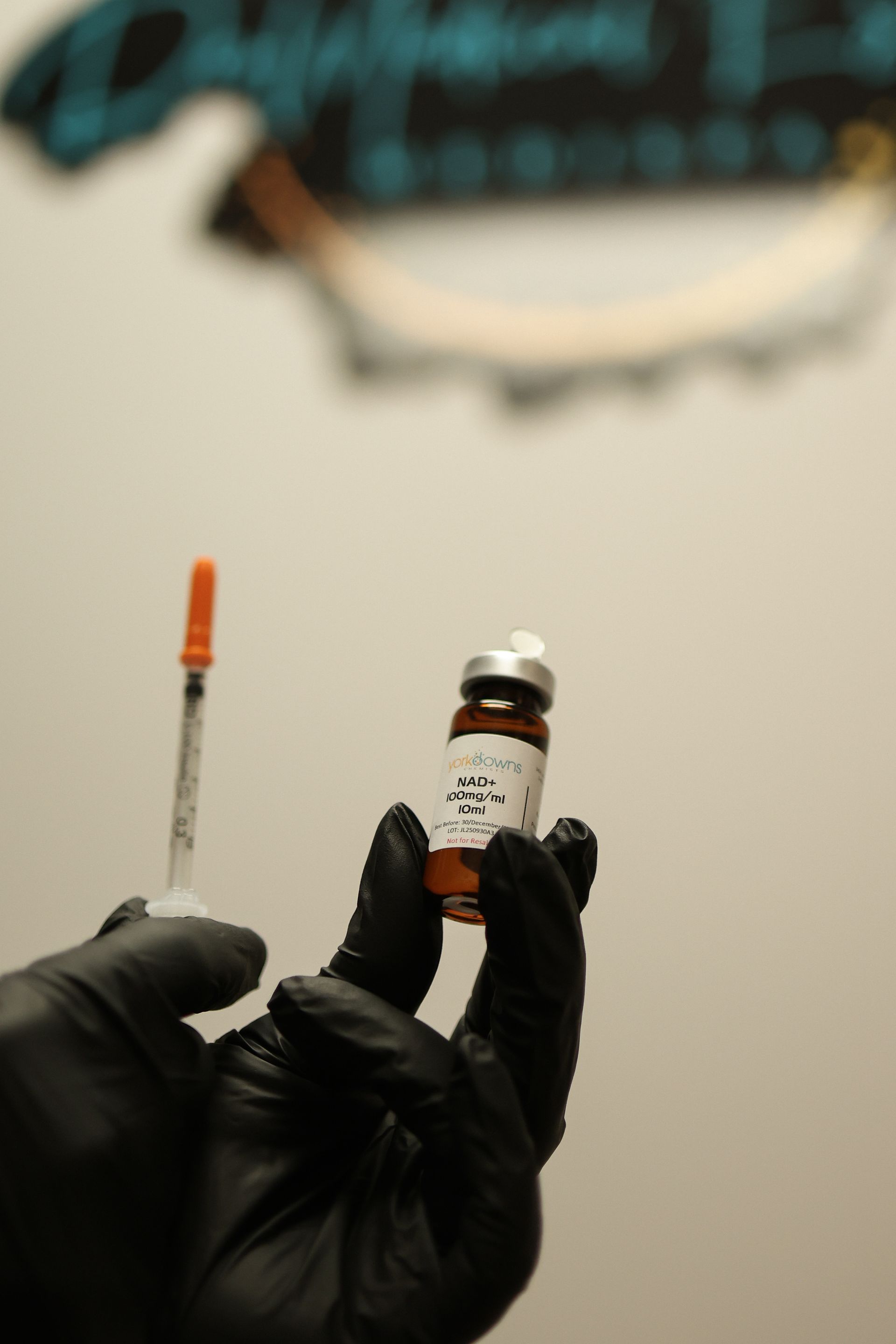 Gloved hand holding vial and syringe with orange cap against a blurry background.