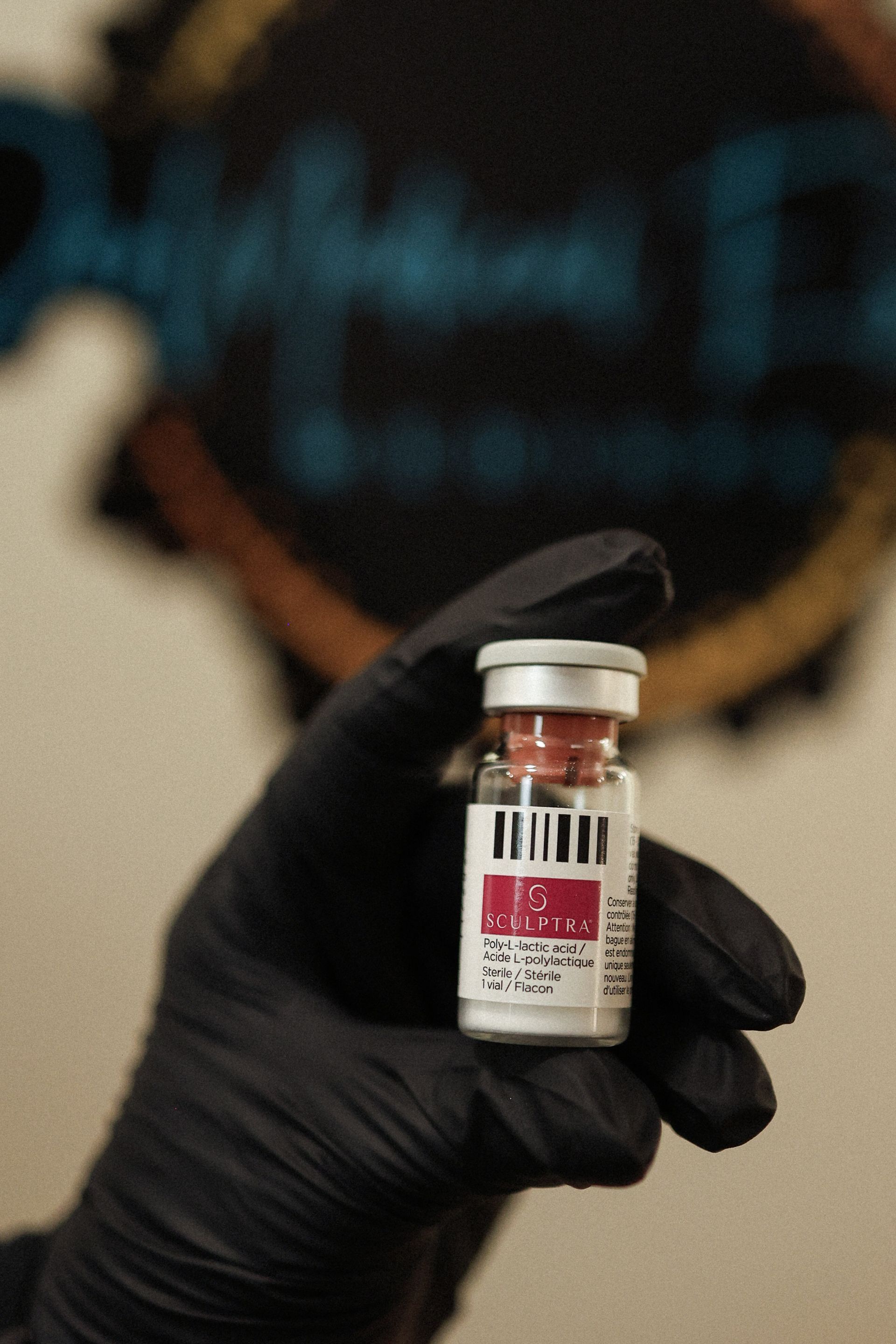 Gloved hand holding a vial with a red top and label against an abstract background.