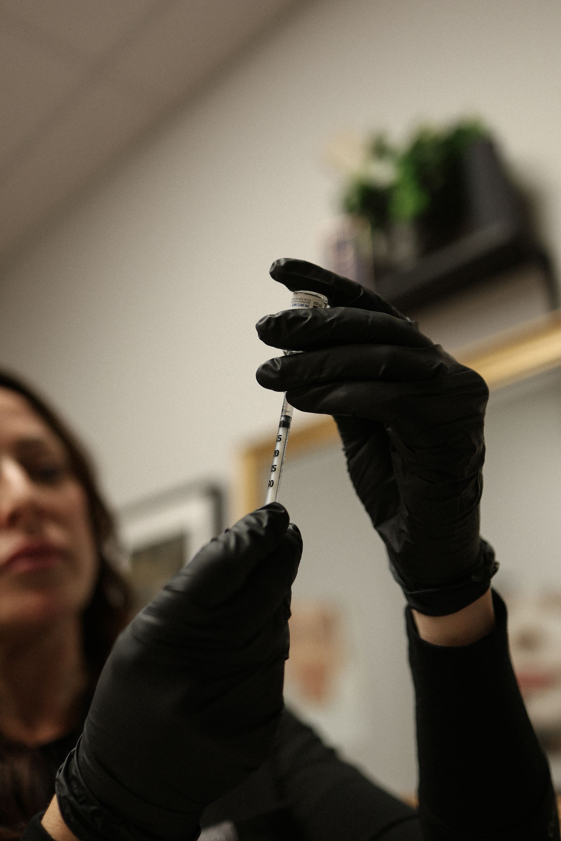 Person in black gloves preparing an injection with a syringe.