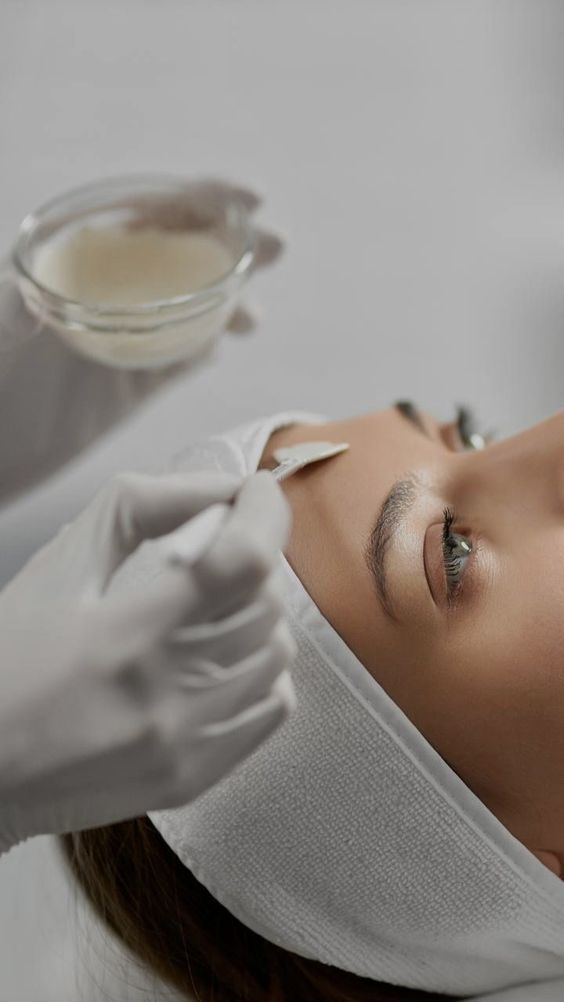 Person receiving facial treatment, applying product to face, hands in gloves, spa setting.