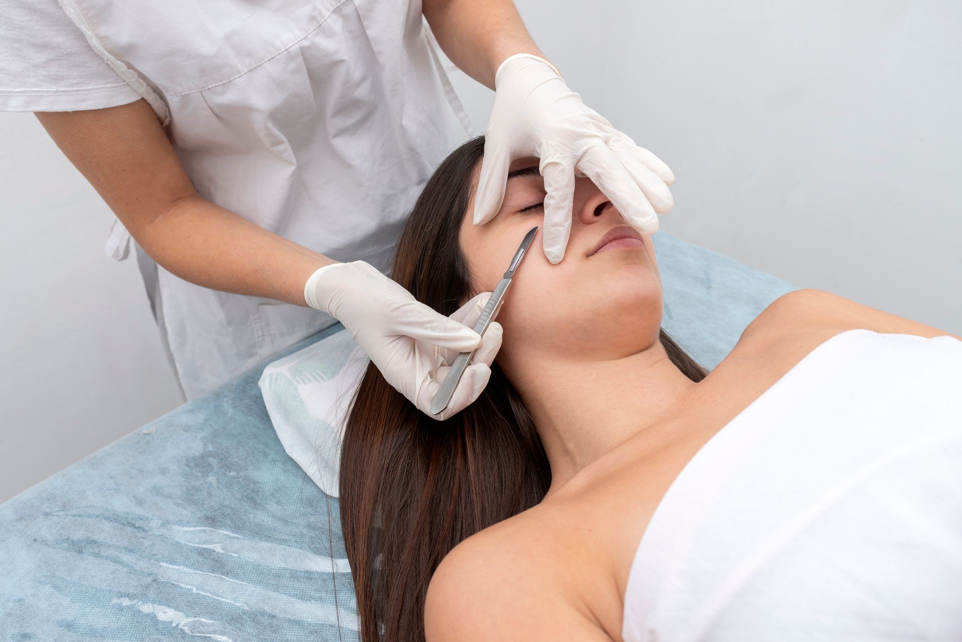 Woman receiving facial procedure with a scalpel. Doctor in gloves performs treatment.