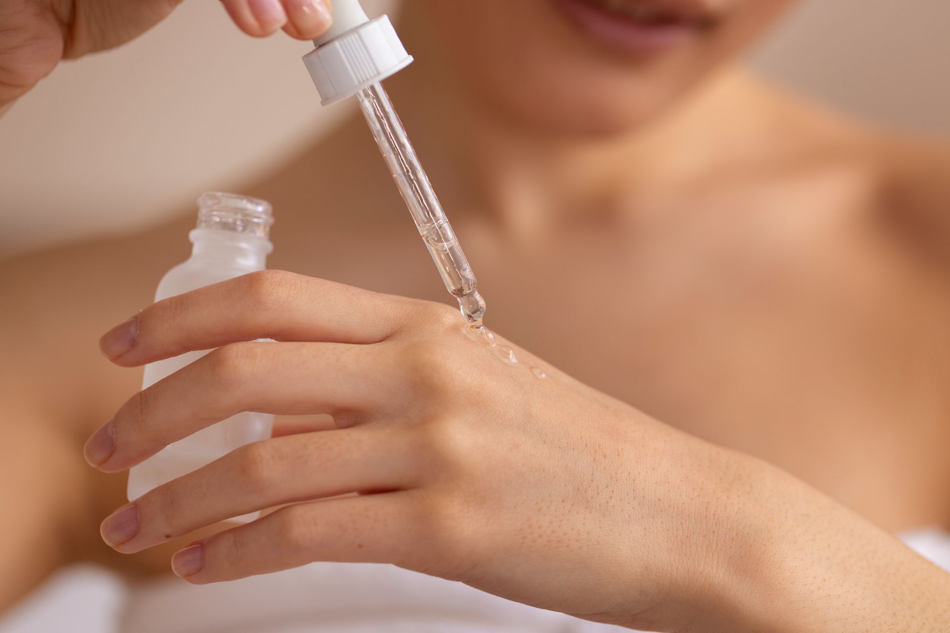 Woman dispensing serum from a dropper bottle onto her hand, close-up.
