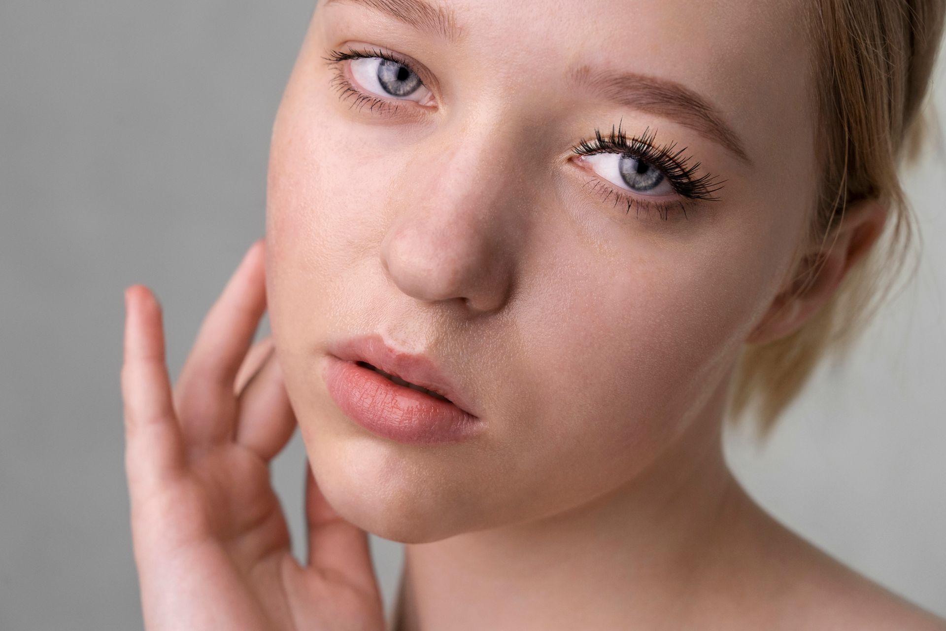 Young woman with pale skin and blue eyes, hand touching her cheek, looking towards the viewer.
