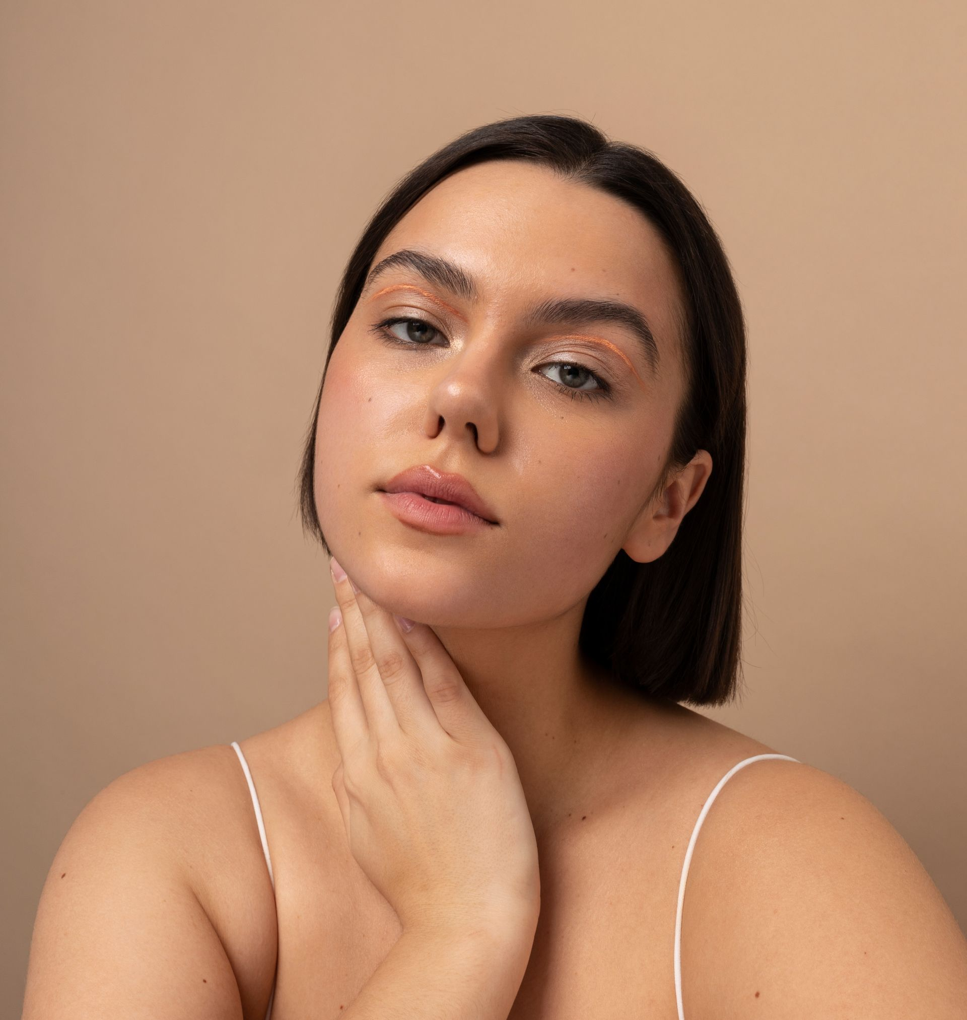 Woman with pale skin, holding her neck, wearing minimal makeup. Light background.