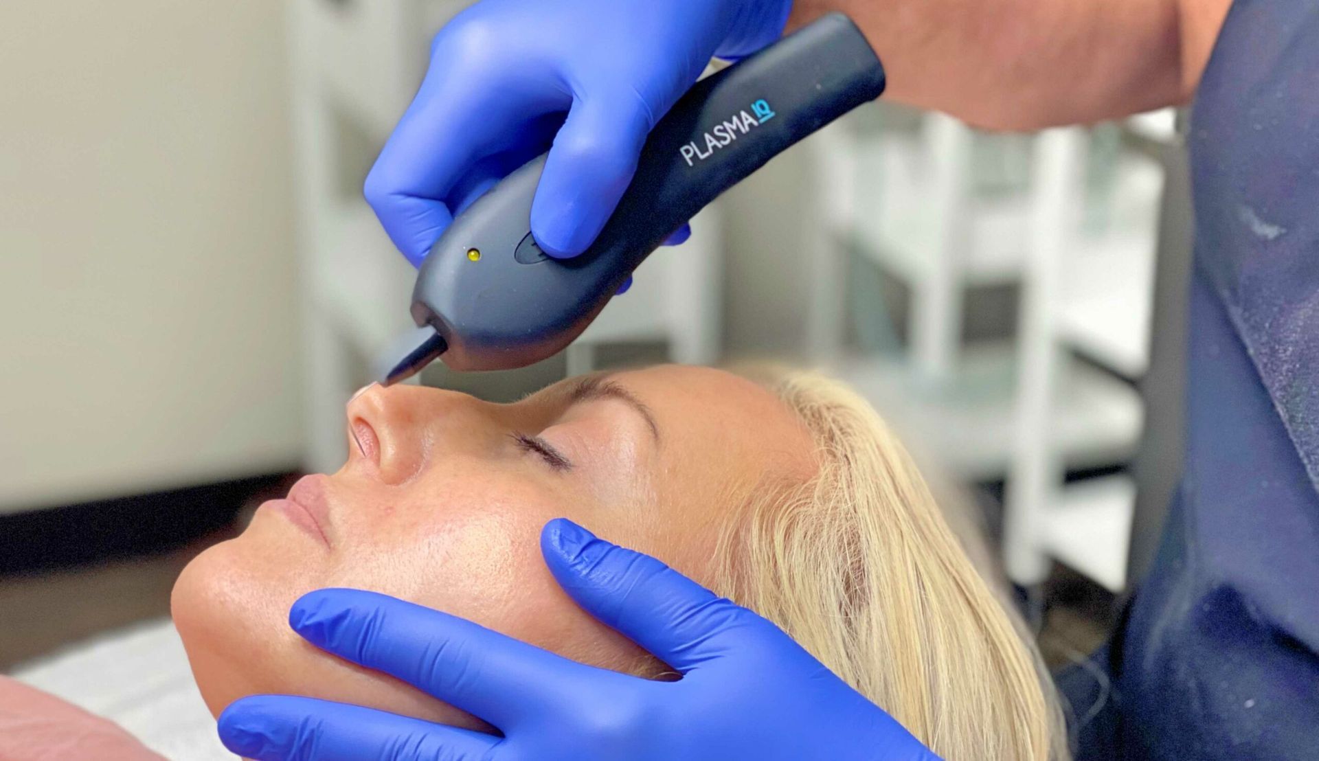 Person receiving Plasma Pen treatment on their nose, indoors. Practitioner in blue gloves.
