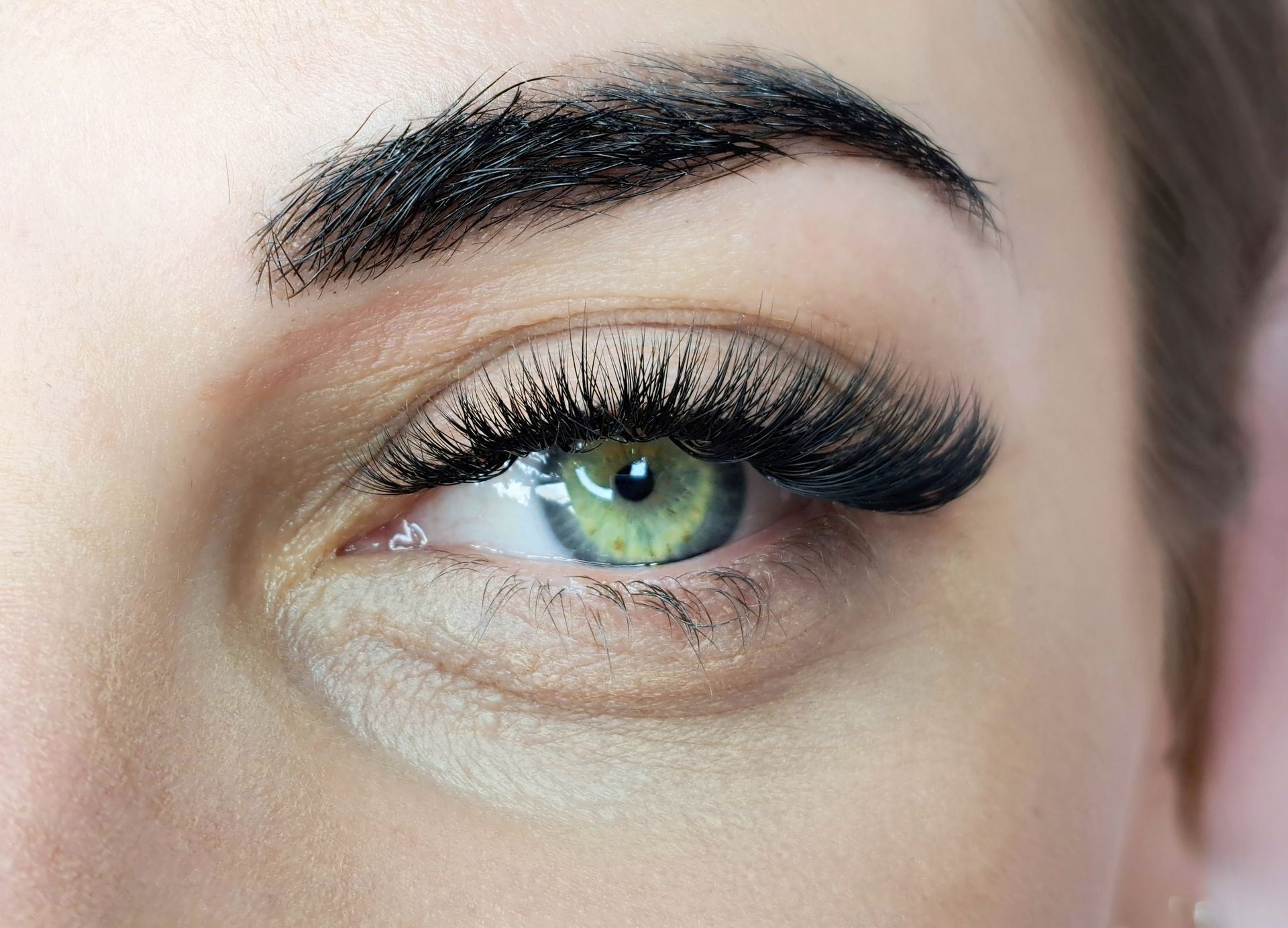 Close-up of an eye with full, dark eyelashes, a defined eyebrow, and a light green iris.