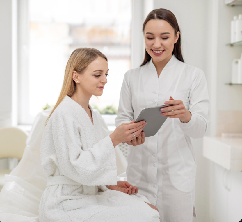 Woman in robe consults with professional, looking at a tablet in a spa setting.