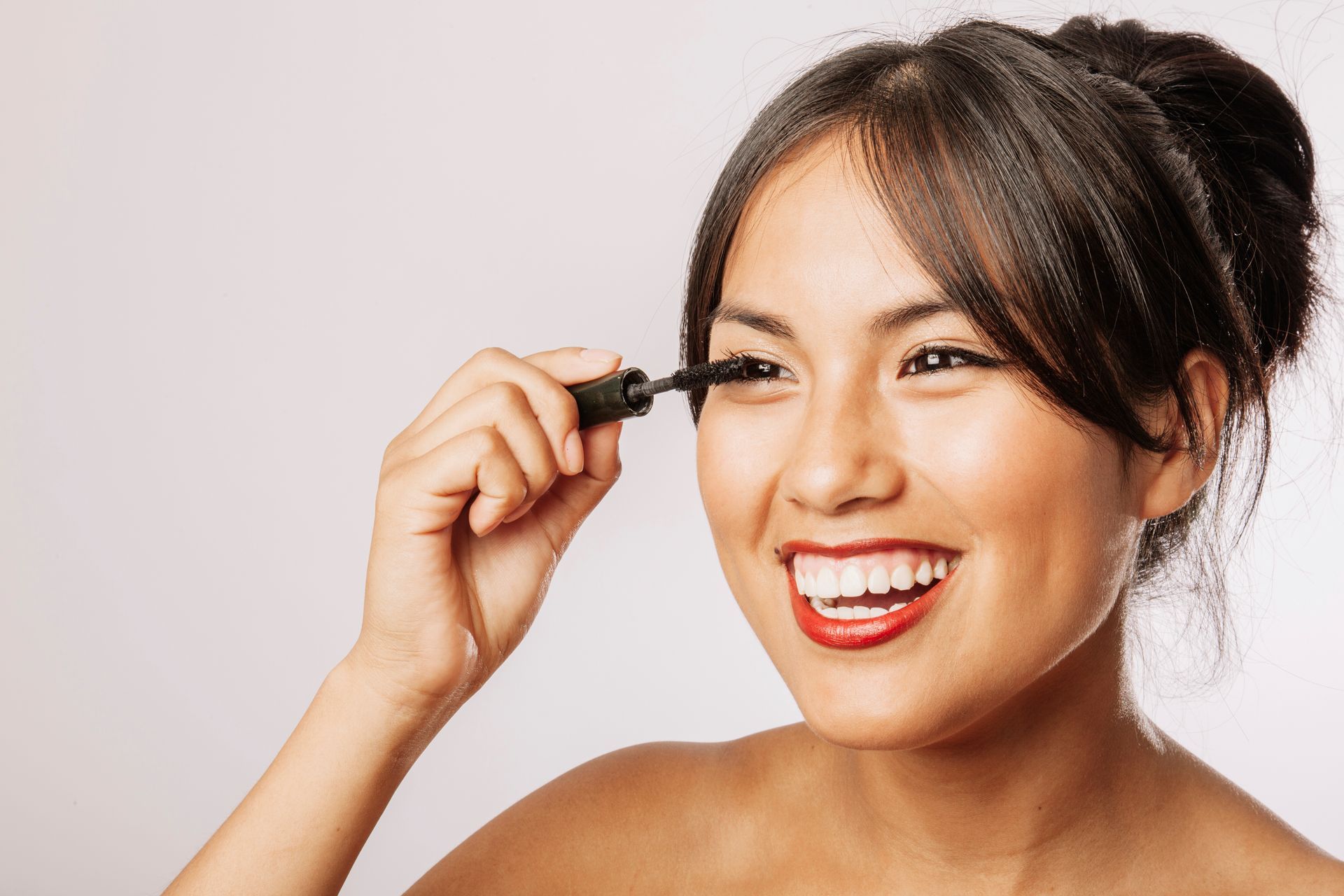 Woman applying mascara, smiling, against a white background.